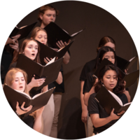 A student choir stands singing while holding their music folders.